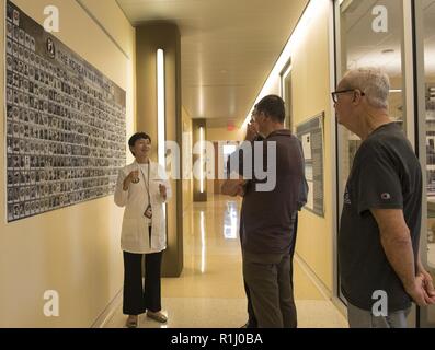 Le Dr Jennie Jin, une défense POW/MIA Agence Comptable (DPAA) anthropologue judiciaire, montre une affiche contenant des photos de la guerre de Corée ont représenté pour le personnel à Larry McDaniel, droite, et Ret. L'ARMÉE AMÉRICAINE Le Colonel Charles McDaniel, Jr., fils du maître Le Sgt. Charles H. McDaniel, un compte récemment pour des héros de guerre, sur une base commune Pearl Harbor-Hickam, New York, le 20 septembre 2018. Les frères se sont rendus à la DPAA laboratory voir le reste de leur père. DPAA mène des recherche globale, de récupération et d'activités de laboratoire afin d'offrir le plus possible notre personnel manquant à leurs familles et th Banque D'Images