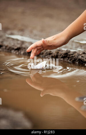 Enfant jouant avec bateau de papier dans une flaque. Banque D'Images