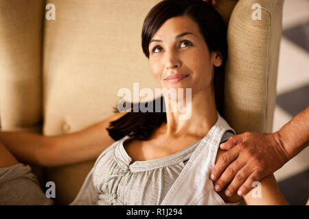 Mid-adult woman relaxing on fauteuil avec un main sur son épaule. Banque D'Images