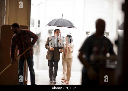 Smiling businessman holding un parapluie pour un collègue. Banque D'Images