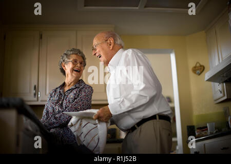 Smiling elderly couple partager un moment d'affection alors qu'ils ne la vaisselle ensemble. Banque D'Images