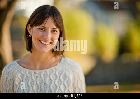 Portrait of a smiling young woman relaxing in a sunlit jardin. Banque D'Images