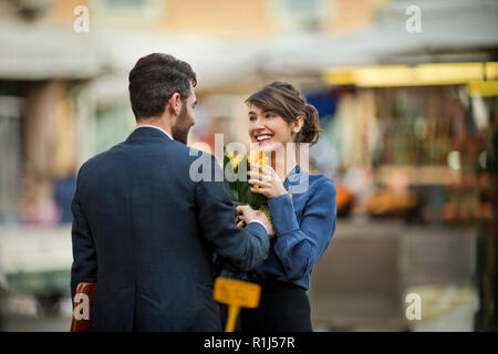 Young businessman présente son collègue avec un groupe de tulipes orange vif. Banque D'Images