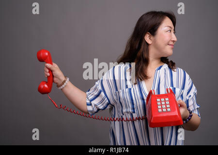 Belle asiatique mature businesswoman holding old red phone Banque D'Images