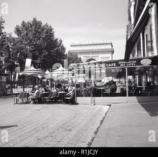 Années 1960, historiques, l'heure d'été et les gens assis dans le bar en plein air, à l'extérieur de la Maison du Café sur les Champs-Elysées, avec le célèbre monument français de l'Arc de Triomphe au loin. Banque D'Images