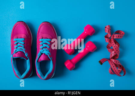 Mise à plat avec rose sneakers, haltères organisé et bande de mesure placés dans la rangée isolé sur bleu, concept minimaliste Banque D'Images