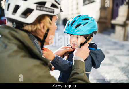 Un jeune père de mettre sur un casque sur la tête de son petit garçon à l'extérieur dans la ville. Banque D'Images