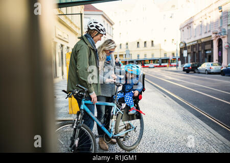 Un petit bébé garçon assis en selle de vélo avec les jeunes parents à l'extérieur dans la ville. Banque D'Images