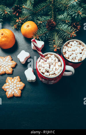 Vue de dessus de tasses de boissons chaudes avec des guimauves, biscuits et de tangerines sur surface noire, petit déjeuner de Noël concept Banque D'Images