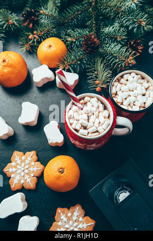 Vue de dessus de tasses de boissons chaudes avec des guimauves, cassette vidéo et de tangerines sur surface noire, petit déjeuner de Noël concept Banque D'Images