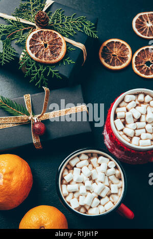 Vue de dessus de tasses de boissons chaudes avec des guimauves, mandarines et des cadeaux de Noël sur surface noire Banque D'Images