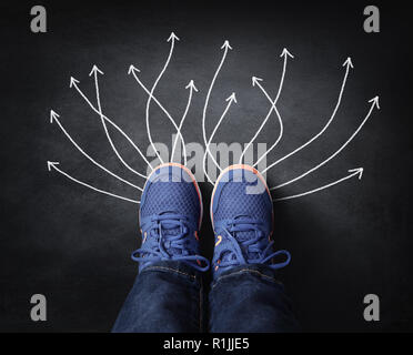 Pieds avec sneakers debout à côté de flèches à la craie sur tableau noir de la prise de décisions pour l'avenir Banque D'Images
