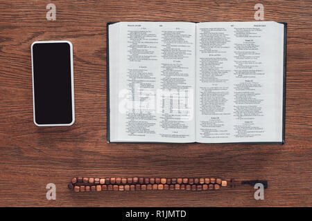 Vue de dessus de la sainte bible ouverte avec perles et smartphone sur table en bois Banque D'Images