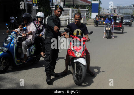 Lhokseumawe, Aceh, Indonésie. 13Th Nov, 2018. L'agent de police de la charia islamique (Wilayatul Hisbah) vu l'arrêt d'un automobiliste vêtu d'un court-circuit au cours de la routine des raids à Lhokseumawe.la charia islamique des fonctionnaires de police (Wilayatul Hisbah) fournir des sarongs pour ceux qui violent la loi de la charia islamique par la force dans la ville de Lhokseumawe, Aceh est la seule province de l'Indonésie qui a la plus grande population de musulmans dans le monde, qui met en œuvre la charia islamique comme la commission de la bastonnade et mener des raids de routine pour ceux qui sont bien habillés pour femmes et des shorts pour hommes. (Ima Crédit Banque D'Images