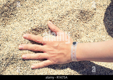 Main femme avec bracelet resort sur le sable Banque D'Images
