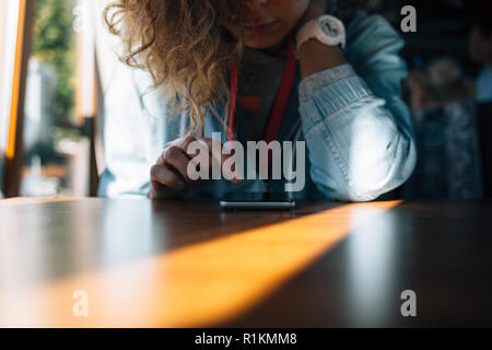 Young woman reading smart phone sitting at table in cafe. Close-up femelle avec de graves pensive expression ressemble à l'appareil mobile de toucher l'écran avec Banque D'Images