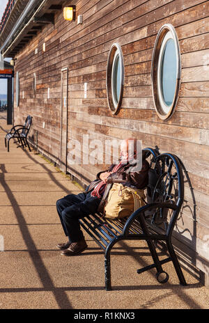 Senior man sleeping au soleil sur la jetée de Southend. Banque D'Images