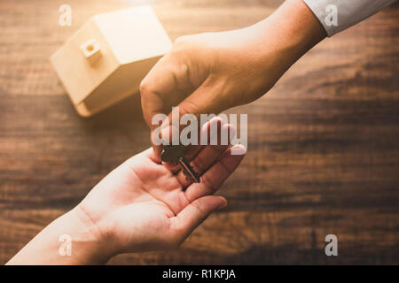 Concept immobilier agence d'accueil, donner la clé de chambre banquier propriétaire ou acheteur sur table en bois dans ton vintage Banque D'Images