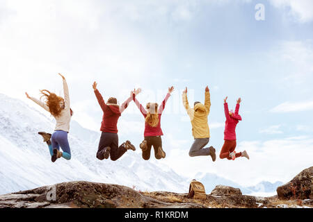 Groupe de cinq amis heureux saute sur le rocher sur fond de montagnes enneigées Banque D'Images