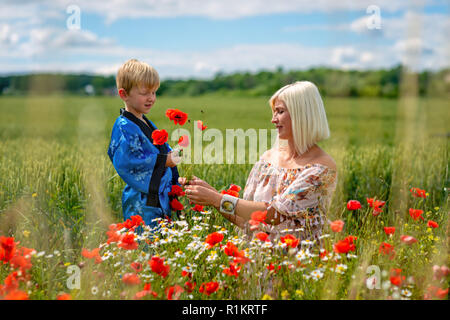 Maman avec son fils dans une magnifique prairie. Le garçon surpris sa mère avec des coquelicots rouges. Banque D'Images