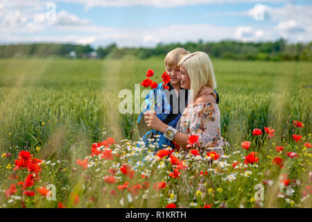 Maman avec son fils dans une magnifique prairie. Le garçon surpris sa mère avec des coquelicots rouges. Banque D'Images