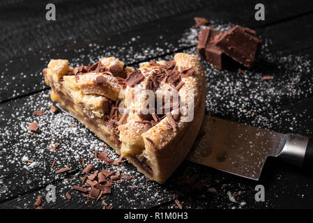 Image en gros plan d'un morceau de tarte aux pommes sur un couteau, décoré avec du sucre en poudre et le chocolat, sur un tableau noir. Délicieux gâteau sucré fait maison. Banque D'Images