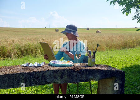 Une dame se trouve à la fin de l'après-midi, l'artiste de l'ombre avec une vue sur la campagne rurale travaillant sur la peinture, elle a commencé plus tôt dans la journée. Banque D'Images