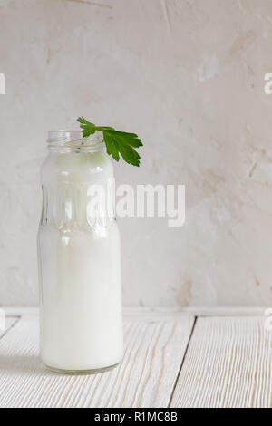 Une bouteille ouverte de kéfir vert avec un brin de persil restant sur la table en bois blanc sur fond blanc avec l'exemplaire de l'espace. Banque D'Images