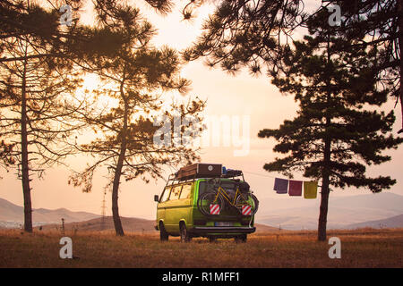 Old Timer le camping-car garé sur le sommet de la colline entre des pins dans le beau ciel de coucher du soleil Banque D'Images