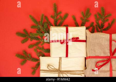 Branches de sapin / brindille et cadeaux de Noël sur fond rouge. Jute et réutilisé/recyclé du papier d'emballage. Ruban Rouge et lin naturel string. Banque D'Images
