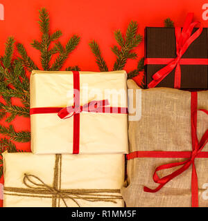 Branches de sapin / brindille et cadeaux de Noël sur fond rouge. Jute et réutilisé/recyclé du papier d'emballage. Ruban Rouge et lin naturel string. Banque D'Images