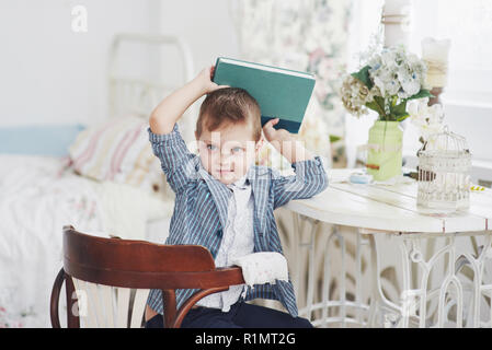 Photo d'écolier diligent avec livre sur sa tête ne veulent étudier et aller à l'école. L'écolier est fatigué de faire leurs devoirs Banque D'Images