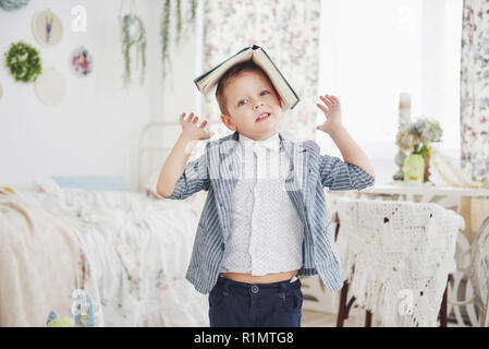 Photo d'écolier diligent avec livre sur sa tête ne veulent étudier et aller à l'école. L'écolier est fatigué de faire leurs devoirs Banque D'Images