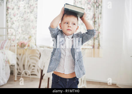 Photo d'écolier diligent avec livre sur sa tête ne veulent étudier et aller à l'école. L'écolier est fatigué de faire leurs devoirs Banque D'Images