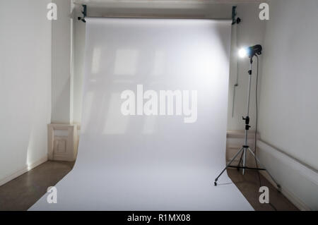 Un studio photo professionnel vide avec propre et simple de configuration de l'équipement photographique, papier ordinaire blanc en toile de fond et un flash lumineux d'une lampe de projecteur sur trépied dans un atelier en grisé Banque D'Images