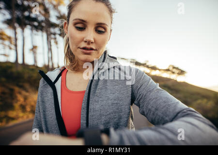 Gros plan d'une athlète féminine vérifiant le temps tout en marchant sur la route. femme de fitness regardant sa montre-bracelet pendant sa promenade de fitness matinale. Banque D'Images