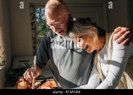 La cuisson des aliments Senior man holding sa femme dans ses bras debout dans la cuisine. Senior couple having bon temps de cuisson des aliments ensemble à la maison. Banque D'Images