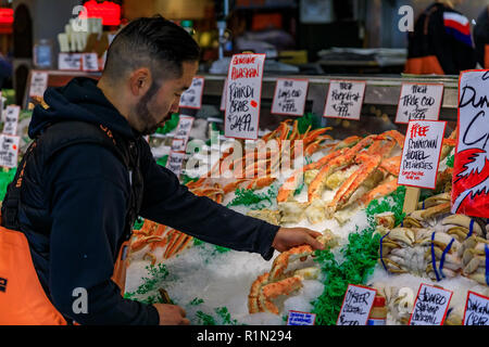 Seattle, États-Unis - Novembre 08, 2018 : poissonnier mettant les pattes de crabe frais sur la glace pour la vente à un décrochage à Pike Place Market avec un client dans le Banque D'Images