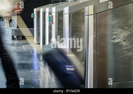 Un homme avec un rouleau à bagages de passer par des portes en acier inoxydable d'un ticket de transport public gare à Paris avec effet de flou. Banque D'Images