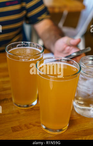 Close up de deux grands verres de bière sur une table dans un restaurant avec personne holding mobile phone in background Banque D'Images