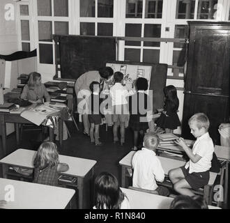 Années 1950, les jeunes enfants avec l'enseignant à l'intérieur d'une pépinière ou jouer-école, en Grande-Bretagne d'après-guerre. Intéressant de voir comment il a été formel, puis une salle de classe avec un bureau approprié mis côte à côte et même un tableau noir. Banque D'Images