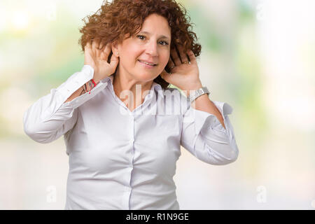 Beau milieu des affaires senior femme ager sur fond isolé essaie d'écouter les deux mains sur le geste de l'oreille, curieux de ragots. Problème d'audition, de Banque D'Images