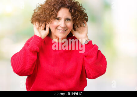 Beau milieu ager senior woman red winter sweater sur fond isolé essaie d'écouter les deux mains sur le geste de l'oreille, curieux de ragots. Audience p Banque D'Images