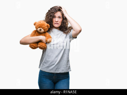 Jeune brunette girl holding nounours plus fond isolé a souligné avec la main sur la tête, choqué par la honte et l'effet de surprise, en colère et frustrés face Banque D'Images