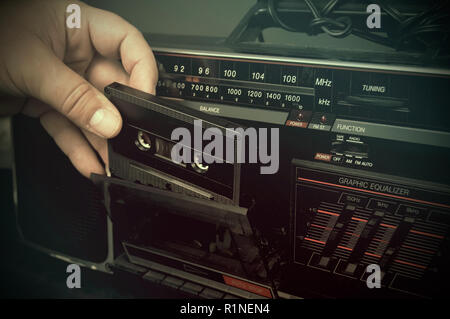 Retro à la photo d'un homme l'insertion d'une cassette dans un vieux lecteur de cassettes poussiéreuses Banque D'Images