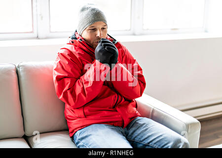 Un homme avec des vêtements chauds sentiment le froid à l'intérieur de maison sur le canapé Banque D'Images