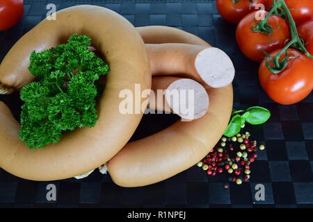 Lyoner est une saucisse fines sur un napperon noir. Lyoner un Wurst-Delikatessen auf einem schwarzen Tischset. Banque D'Images