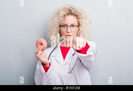 Jeune blonde dietist médecin femme de plus grunge grey wall eating pointant avec le doigt à la caméra et à la main, vous signe, positif et confiant Banque D'Images