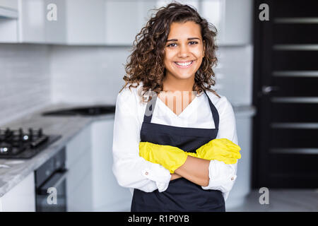 Young Woman smiling woman wearing apron et des gants en caoutchouc, debout dans la cuisine Banque D'Images