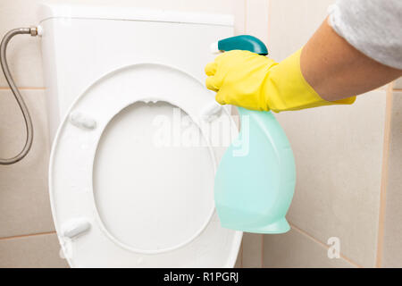 Personne au siège de toilette blanc de pulvérisation et le réservoir jaune portant des gants sanitaires comme concept de nettoyage Banque D'Images